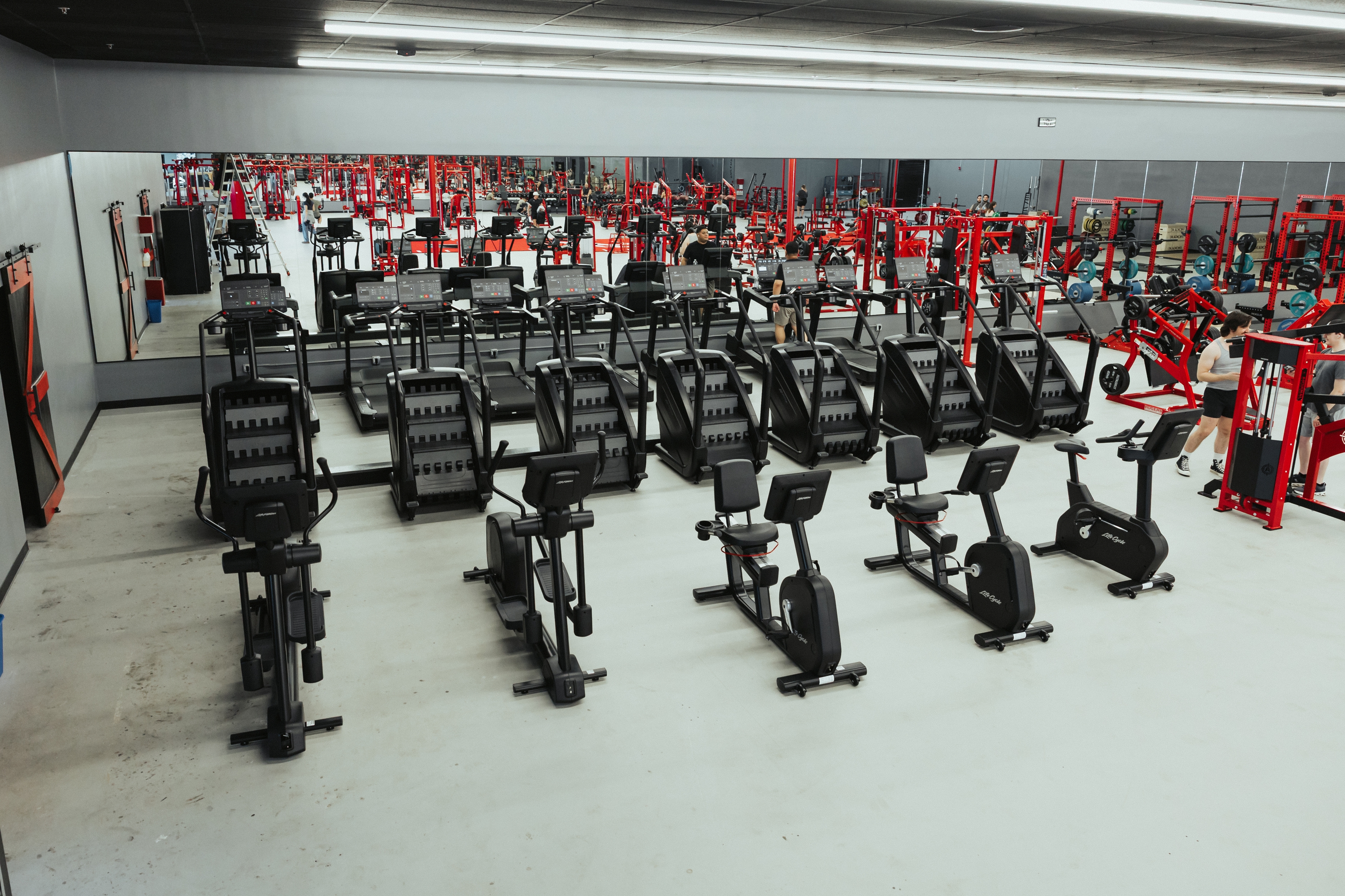 Rows of steppers, treadmills, ellipticals and bikes in the cardio section, with the red strength floor behind
