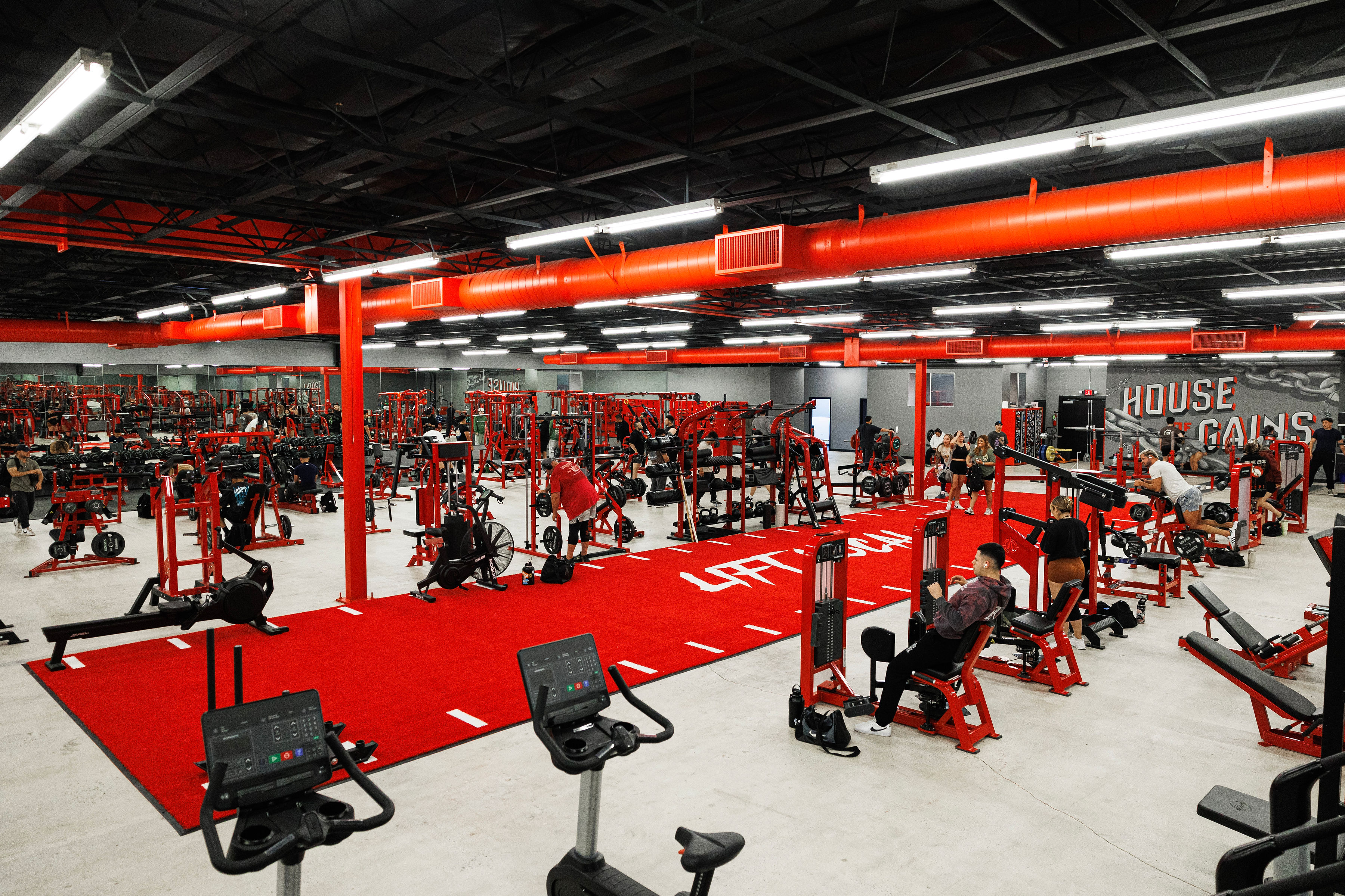 The Oxnard main floor — rows of red racks and machines, the LIFT LOCAL turf lane down the center and the HOUSE OF GAINS mural on the far wall